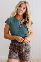 Woman wearing a teal top and leopard print shorts against a light background