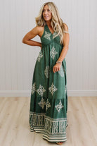 Woman wearing a green dress with white patterns against a light wooden floor and white wall background
