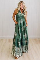 Woman wearing a green floral dress standing against a white wall.