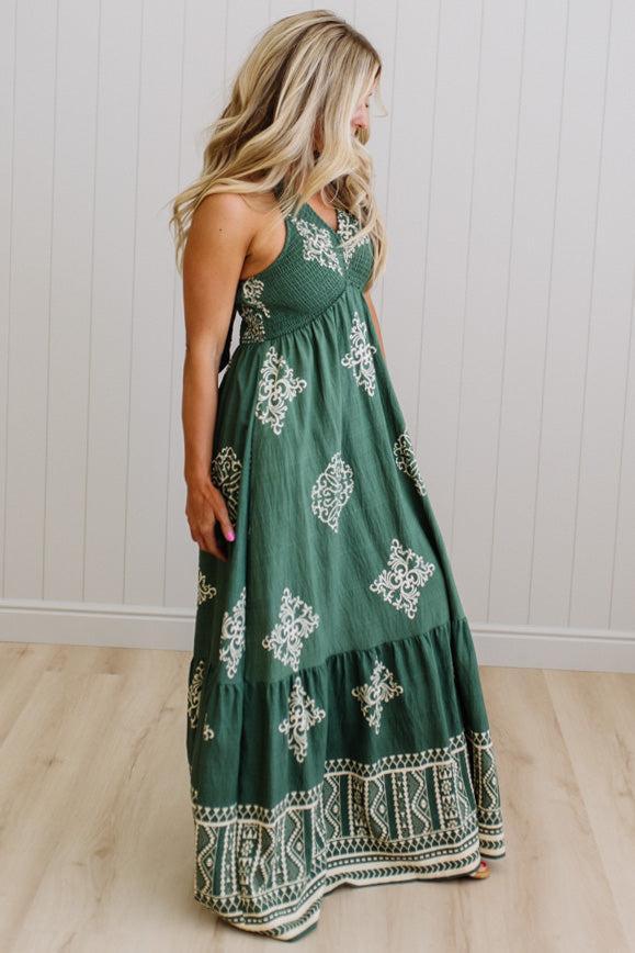 Woman wearing a green dress with white patterns in a room with a wooden floor and white walls.