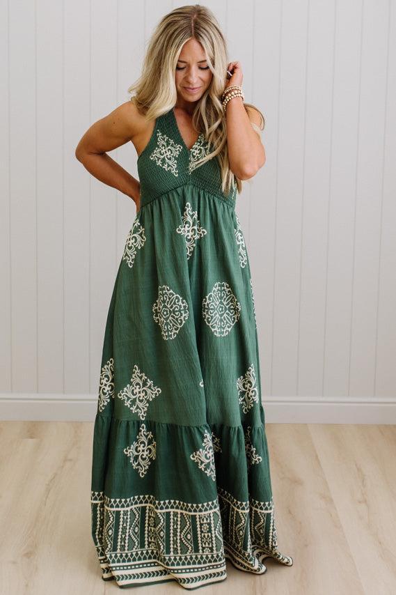 Woman wearing a green dress with white patterns in a room with a white wall and wooden floor.