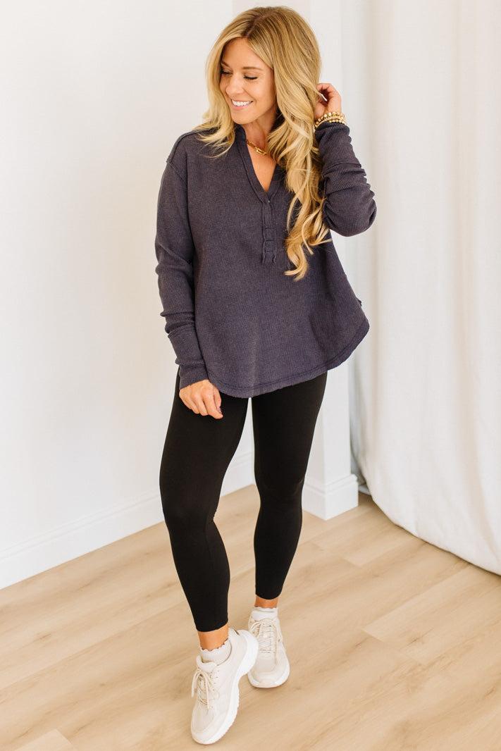 Woman wearing a dark navy long-sleeve top and black leggings, standing indoors.