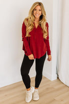 Woman wearing a red long-sleeve top and black leggings indoors.