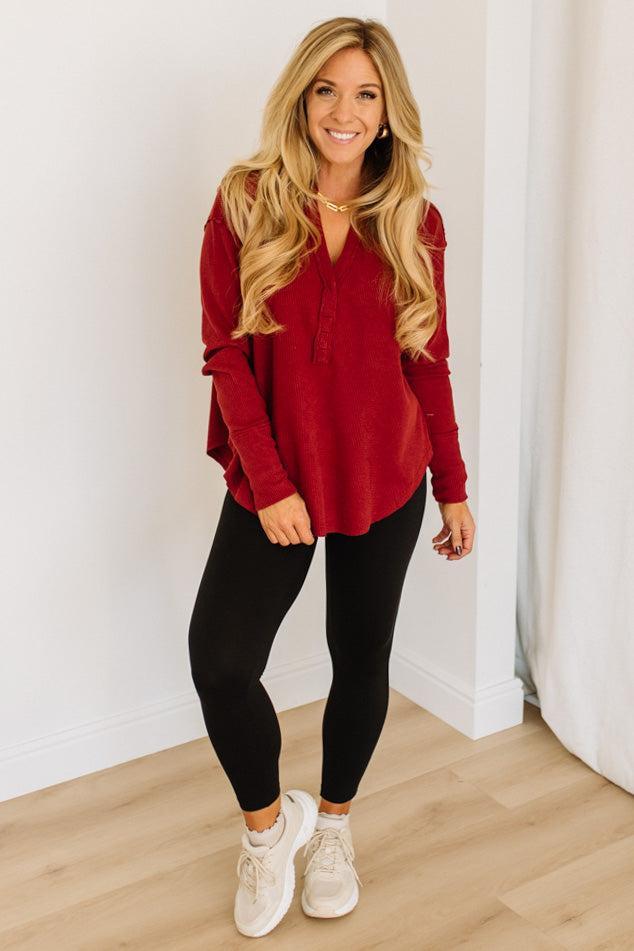 Woman wearing a red long-sleeve top and black leggings indoors.