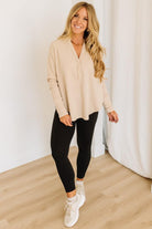 Woman wearing a beige top and black leggings standing in a room with white curtains.