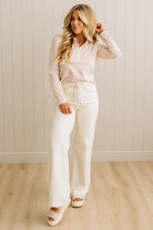 Woman wearing a striped shirt and white pants standing against a light wooden paneled wall.