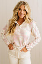 Woman wearing a striped long-sleeve top and white pants against a plain background