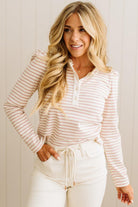 Woman wearing a striped long-sleeve top and white pants against a plain background