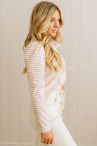 Woman wearing a striped shirt and white pants against a beige wall