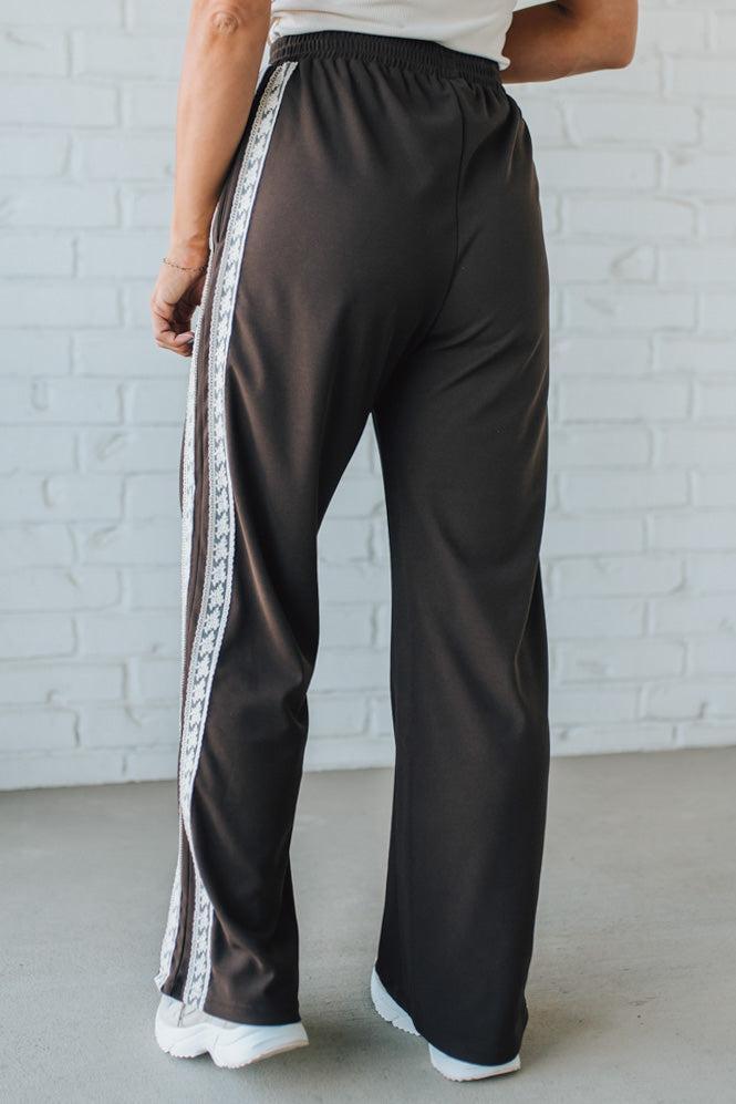 Black pants with white side stripes worn by a person against a light gray brick wall.