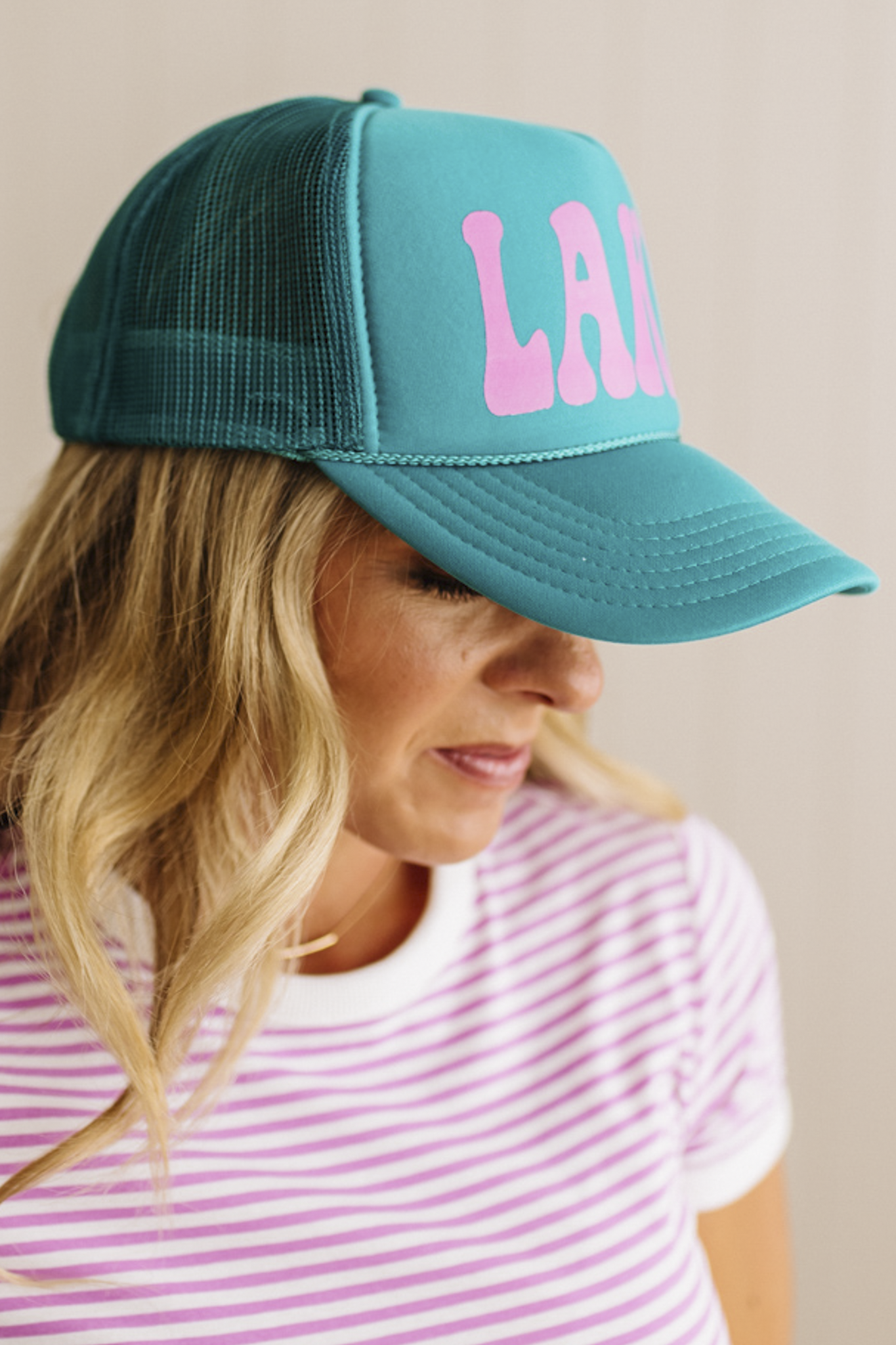 Person wearing a teal cap with pink text on a neutral background