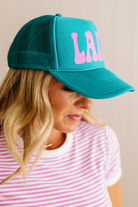 Person wearing a teal cap with pink text on a neutral background