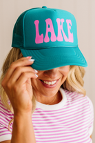 Person wearing a teal cap with 'LAKE' in pink letters, smiling.