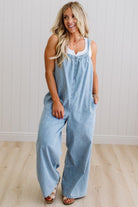 Woman wearing a light blue denim jumpsuit against a white wall.