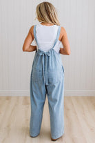 Person wearing a denim overalls with a white top against a light wooden floor and wall background