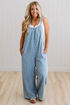 Woman wearing a light blue denim jumpsuit against a white wall.