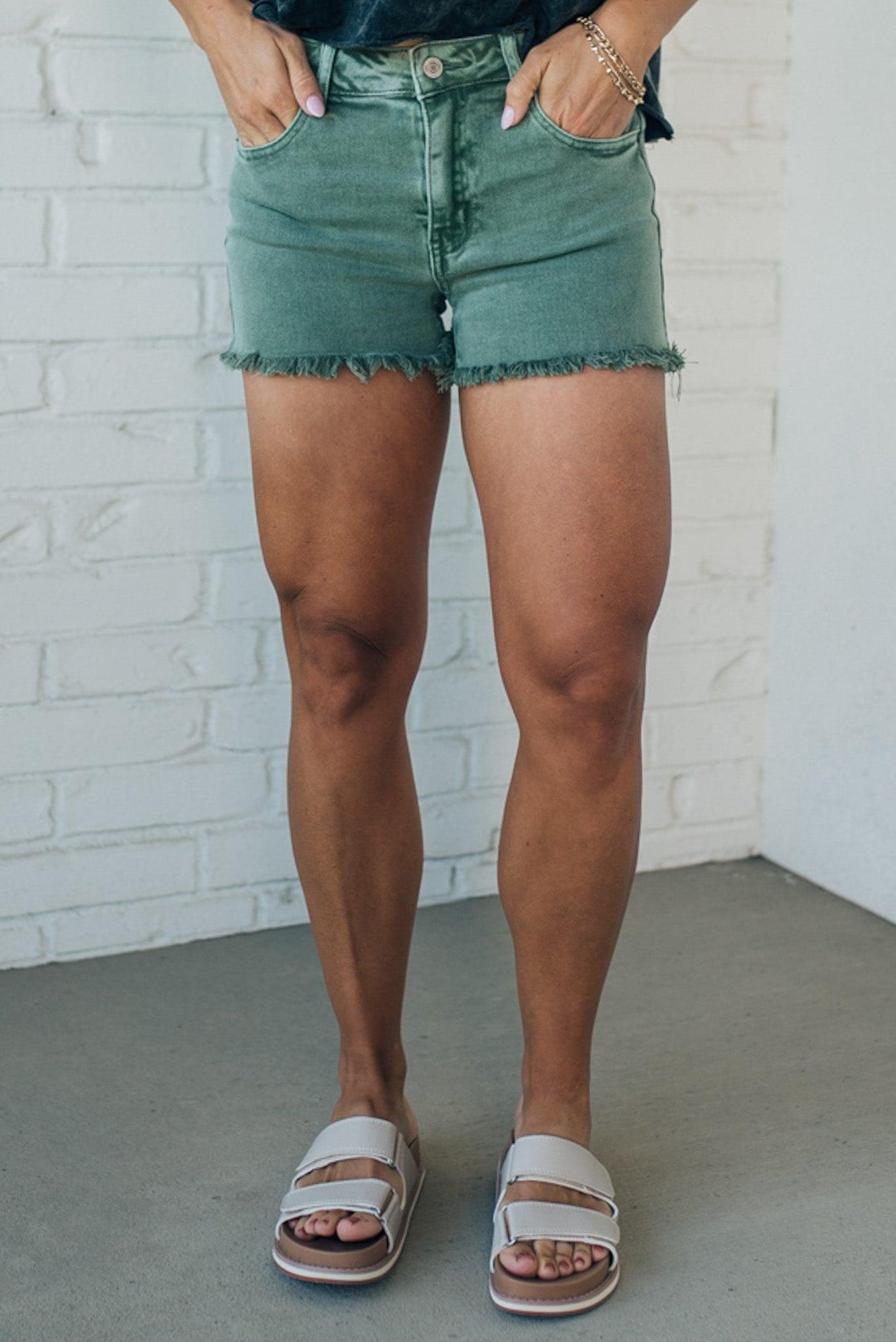 women wearing mid rise frayed shorts that have an olive green mineral wash finish