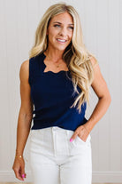 Woman wearing a navy sleeveless top and white pants against a light background