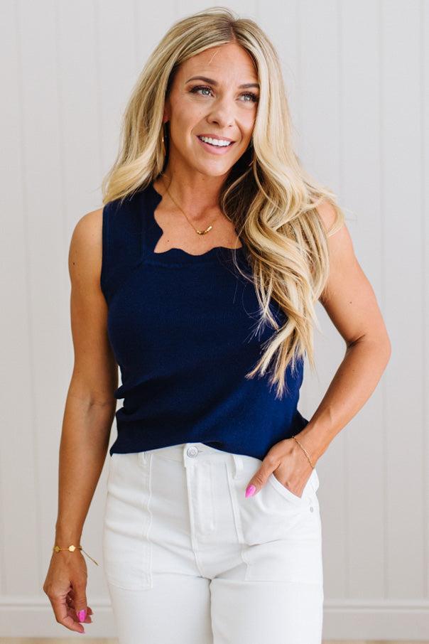 Woman wearing a navy sleeveless top and white pants against a light background