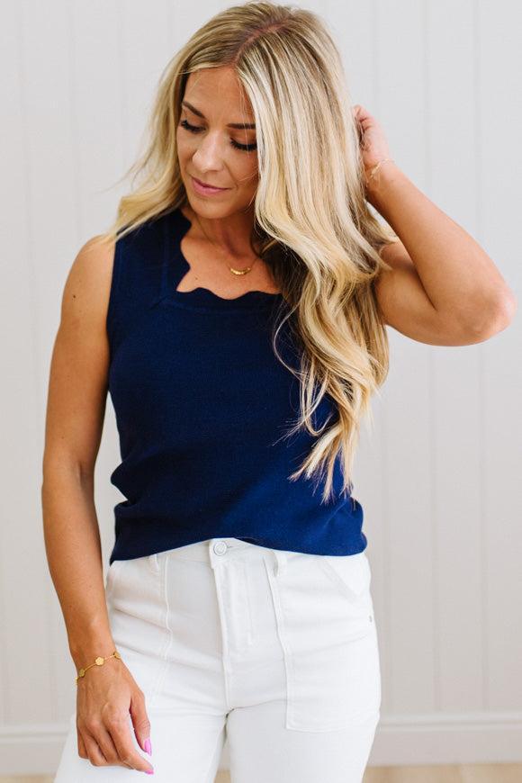 Woman wearing a navy sleeveless top and white pants against a light background