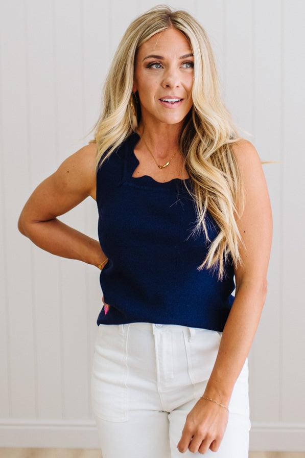 Woman wearing a navy top and white pants against a light background