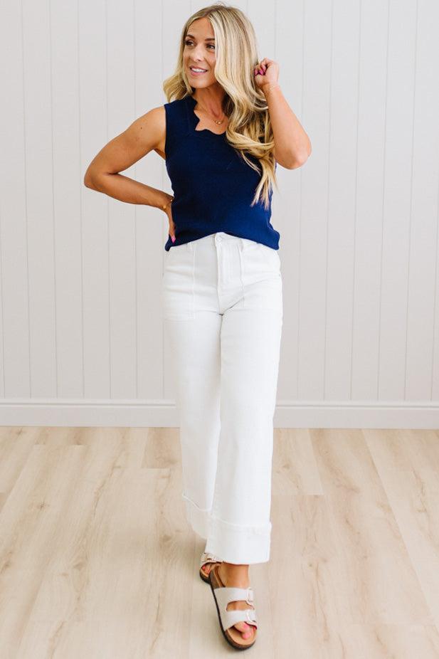 Woman wearing a navy top and white pants against a light wooden floor and wall background