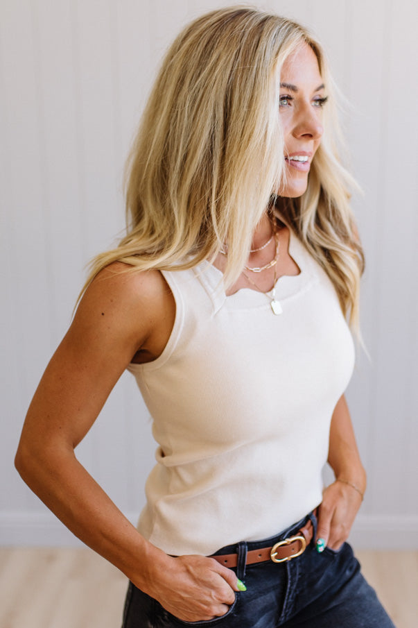 Woman wearing a white sleeveless top and dark jeans against a plain background