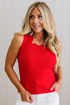 Woman wearing a red sleeveless top and white pants against a light background
