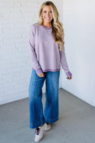 Blonde woman against a white wall wearing a lavender and white striped sweater with blue jeans and sneakers.