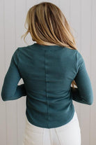 Person wearing a teal long-sleeve top against a light wooden panel background