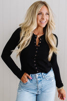 Woman wearing a black long-sleeve top and blue jeans against a plain background