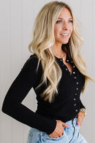 Woman wearing a black long-sleeve top with button details against a light background