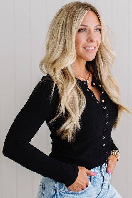 Woman wearing a black long-sleeve top with button details against a light background