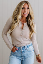 Woman wearing a beige long-sleeve top and blue jeans against a light background