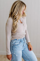 Woman wearing a beige long-sleeve top and light blue jeans against a neutral background