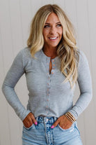 Woman wearing a gray long-sleeve shirt and blue jeans with a neutral background