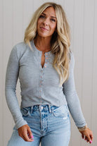 Woman wearing a gray long-sleeve shirt and blue jeans against a neutral background