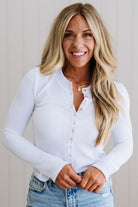 Woman wearing a white long-sleeve shirt and blue jeans against a plain background
