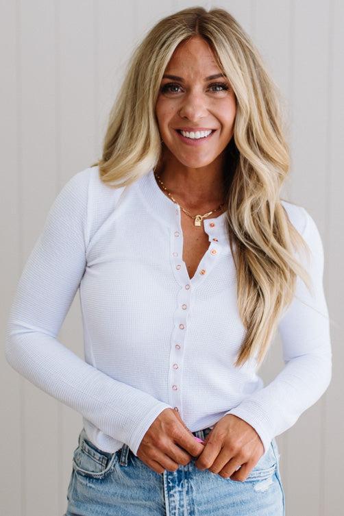 Woman wearing a white long-sleeve shirt and blue jeans against a plain background