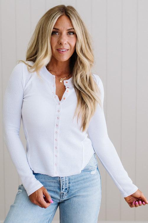 Woman wearing a white long-sleeve shirt and light blue jeans against a neutral background