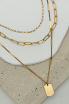 Three strand gold necklace with different chains, and one tag charm.