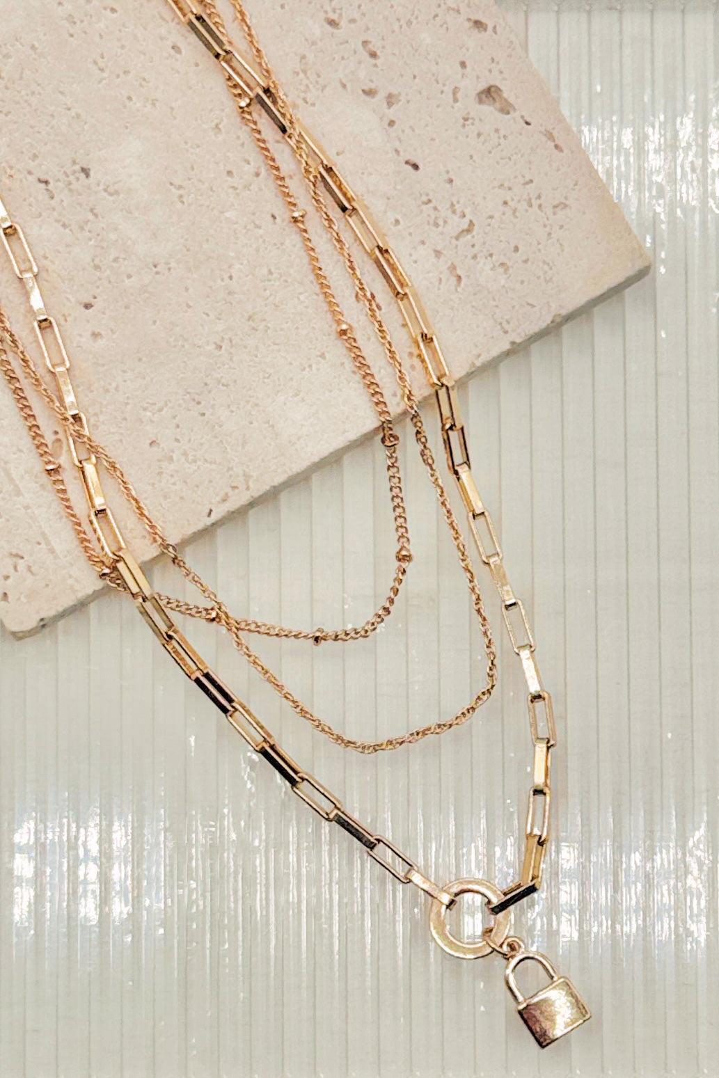 Gold chain necklace with a lock pendant on a textured surface