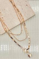Gold chain necklace with a lock pendant on a textured surface