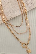 Gold chain necklace with a lock charm on a textured surface