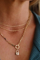 Close-up of a person wearing a gold chain necklace with a lock pendant.