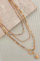 Gold chain necklace with a lock pendant on a textured surface