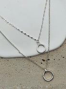 Two silver necklaces with circular pendants on a concrete surface.