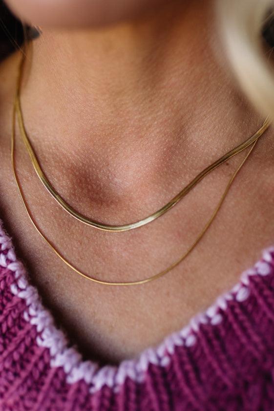 Close-up of a person wearing a gold necklace with a pink sweater.