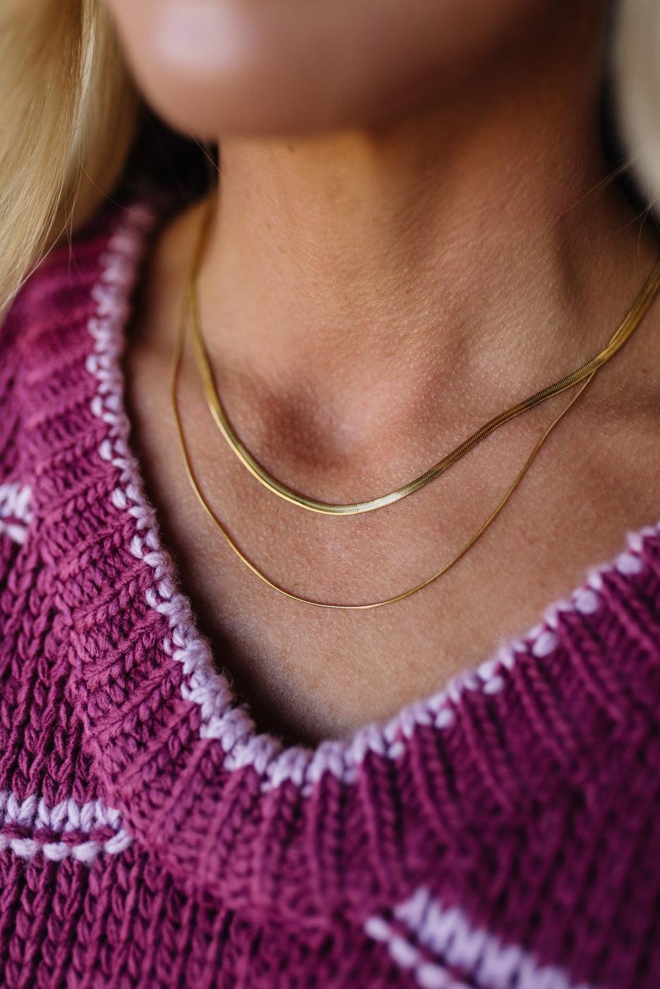 Close-up of a person wearing a gold necklace with a pink sweater.
