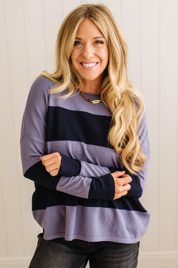 Woman wearing a purple and black striped sweater against a white wall